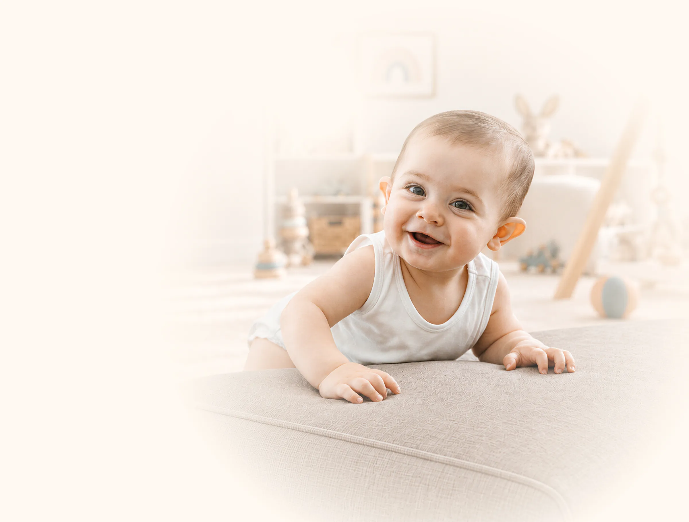 Lachendes Baby stützt sich auf ein helles Sofa, im Hintergrund ein ruhiges Kinderzimmer (vorläufiges Motiv)